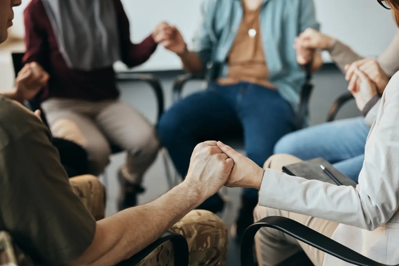 Group therapy: a group of people sitting and holding hands in a circle during group therapy