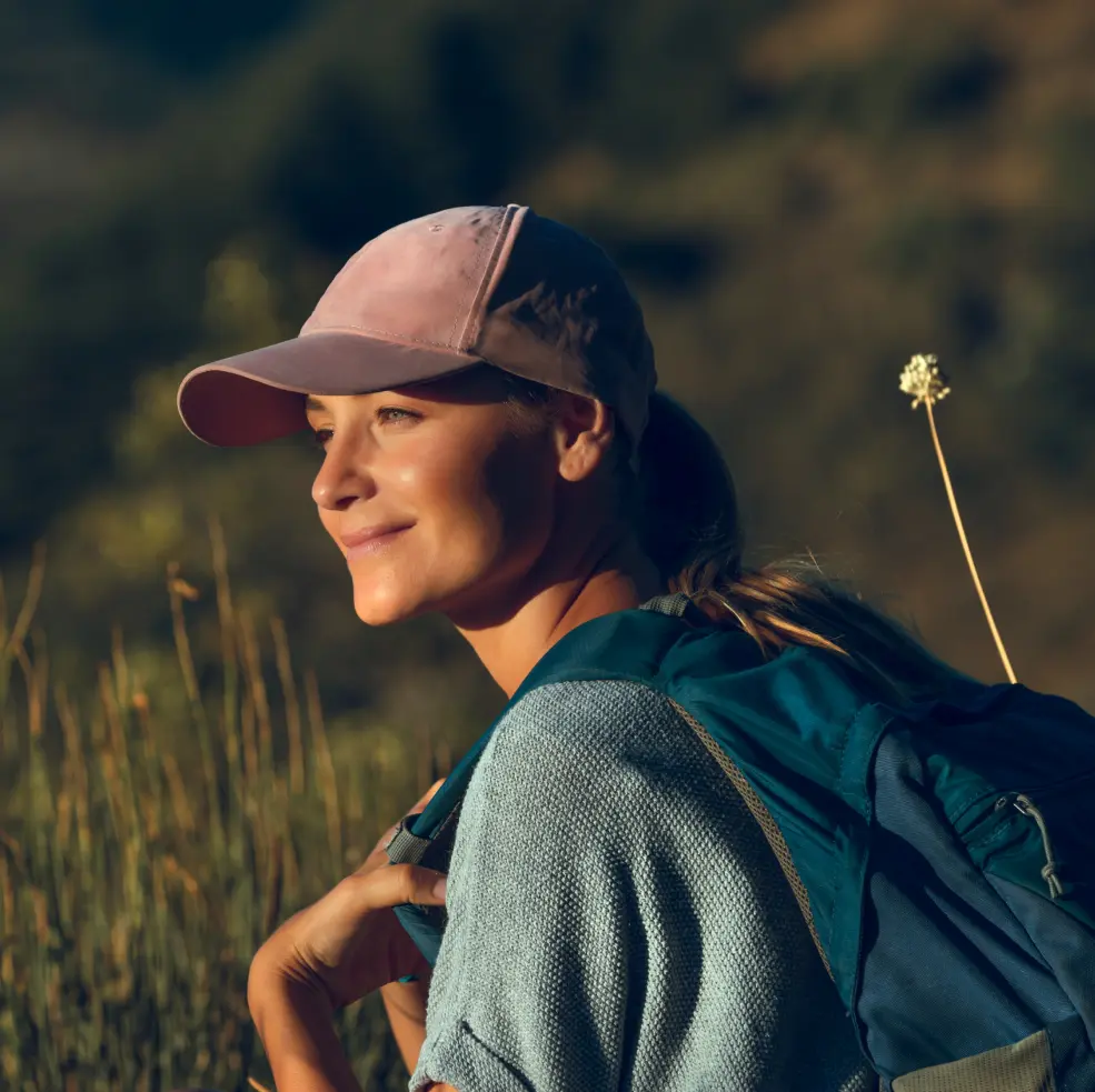 Woman taking a hike in nature wearing a pink baseball cap and blue backpack
