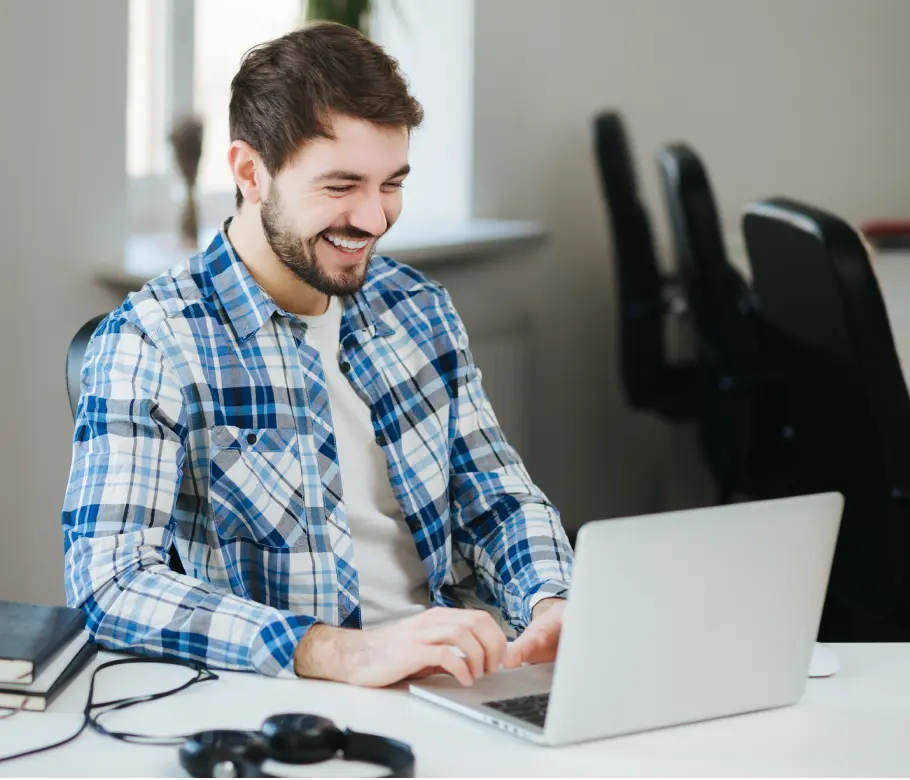 Man in a blue plaid shirt smiling at his laptop while making an appointment