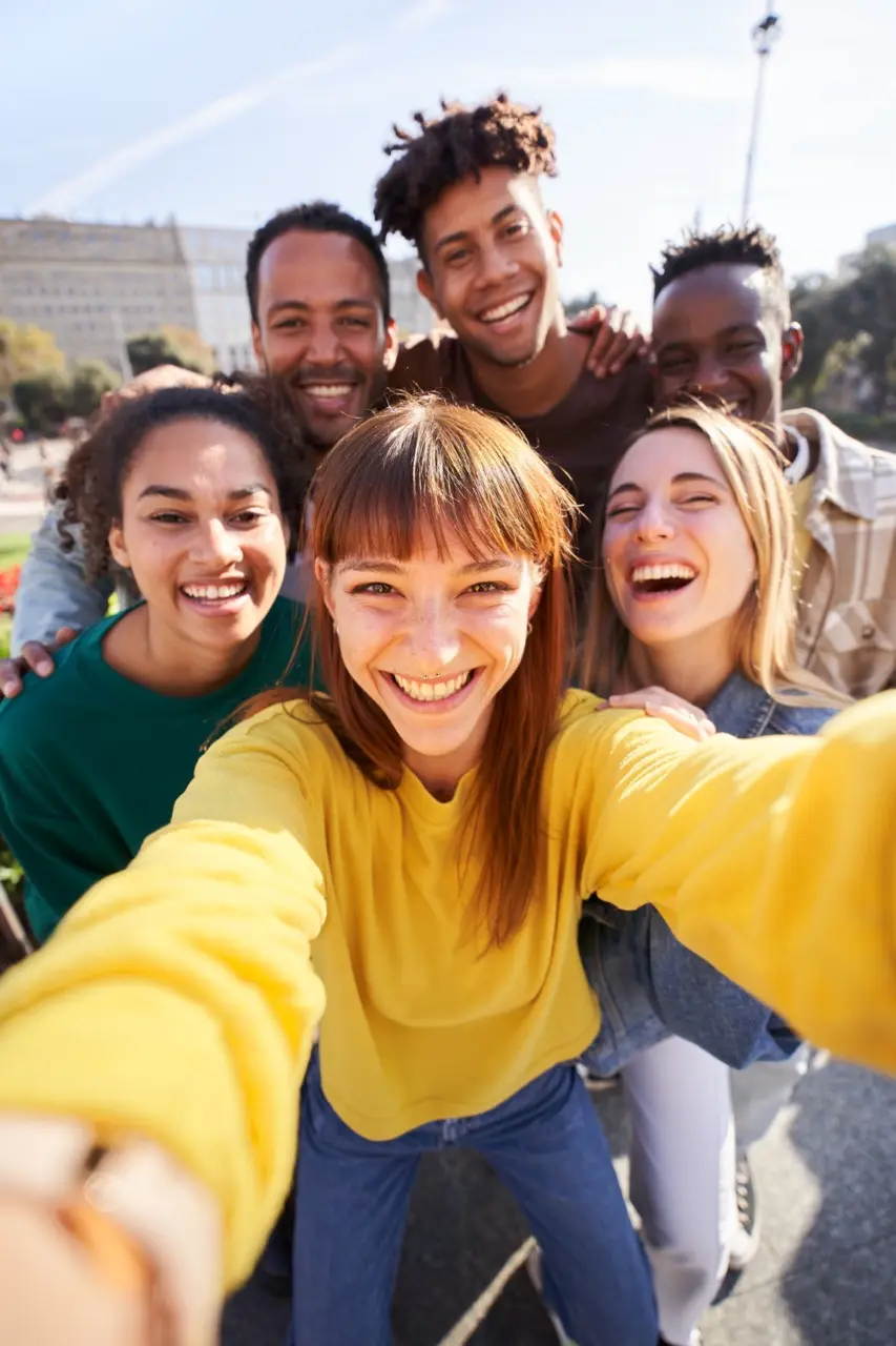 A group of friends from multi-ethnic backgrounds taking a selfie together in front of a building, laughing and smiling